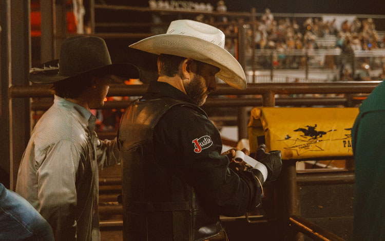 Un hombre con camisa negra y sombrero de vaquero, de pie y prepar&aacute;ndose en un rodeo.